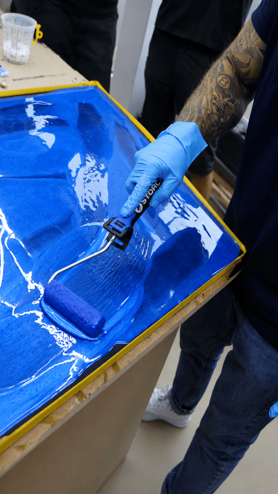 Transparente Versiegelung wird im Epoxidharz-Workshop mit einer Rolle auf eine blaue Metallic-Musterplatte aufgetragen.