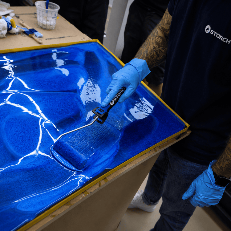 Eine Hand streicht eine MDF Platte mit einem blauen Farbroller in Blau