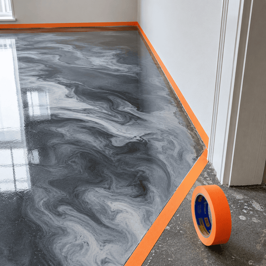Orangenes Klebeband klebt auf am Rand eines grau beschichteten Boden zum Abkleben der Ränder