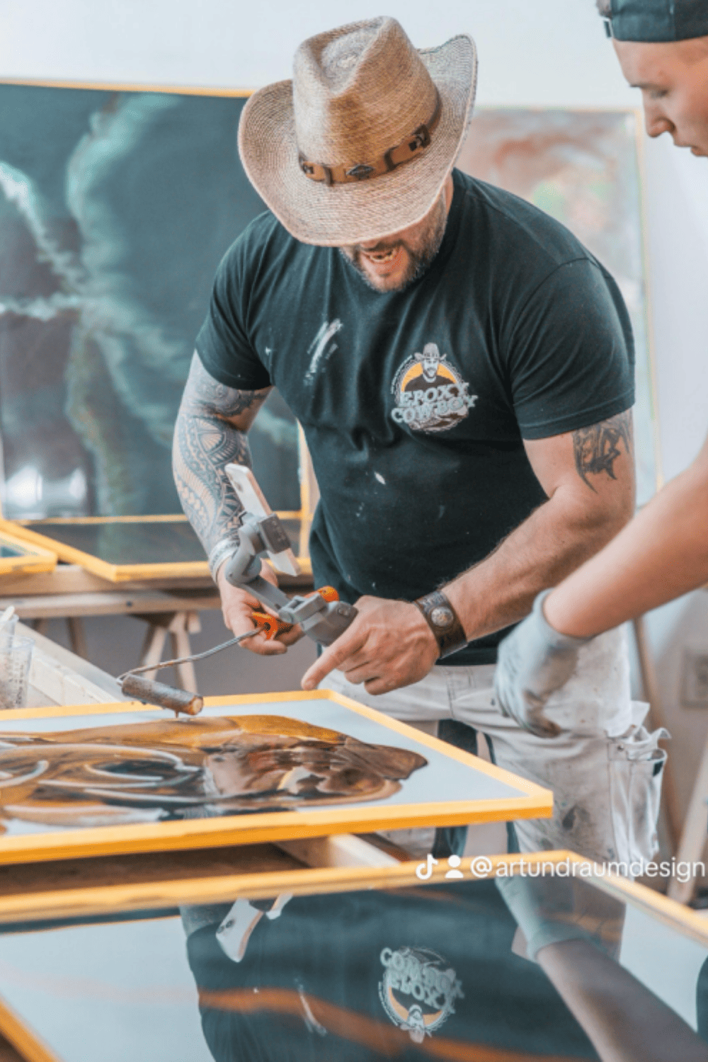Teilnehmer eines Epoxidharz-Workshops gestaltet mit Rolle und Heißluftgerät eine braun-schwarze Metallic-Epoxidharz-Musterplatte.