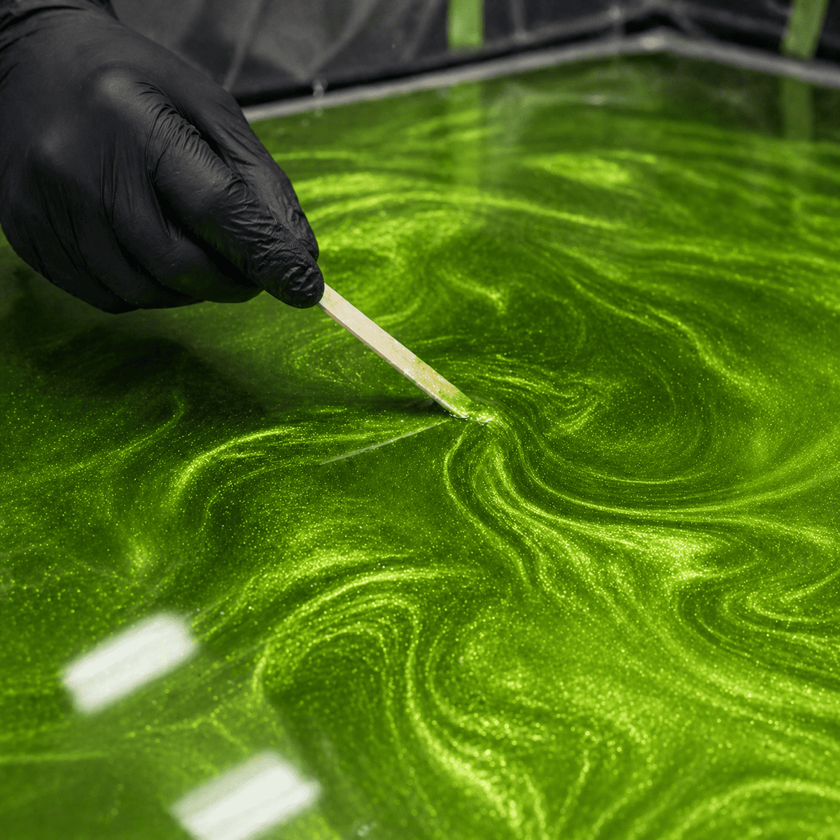 Apple Green UV Metallic-Epoxidharz wird mit einem Holzspatel zu einer dynamischen Marmorstruktur mit brillantem Perleffekt, leuchtendem Apfelgrün-Schimmer und faszinierender Tiefenwirkung gestaltet.