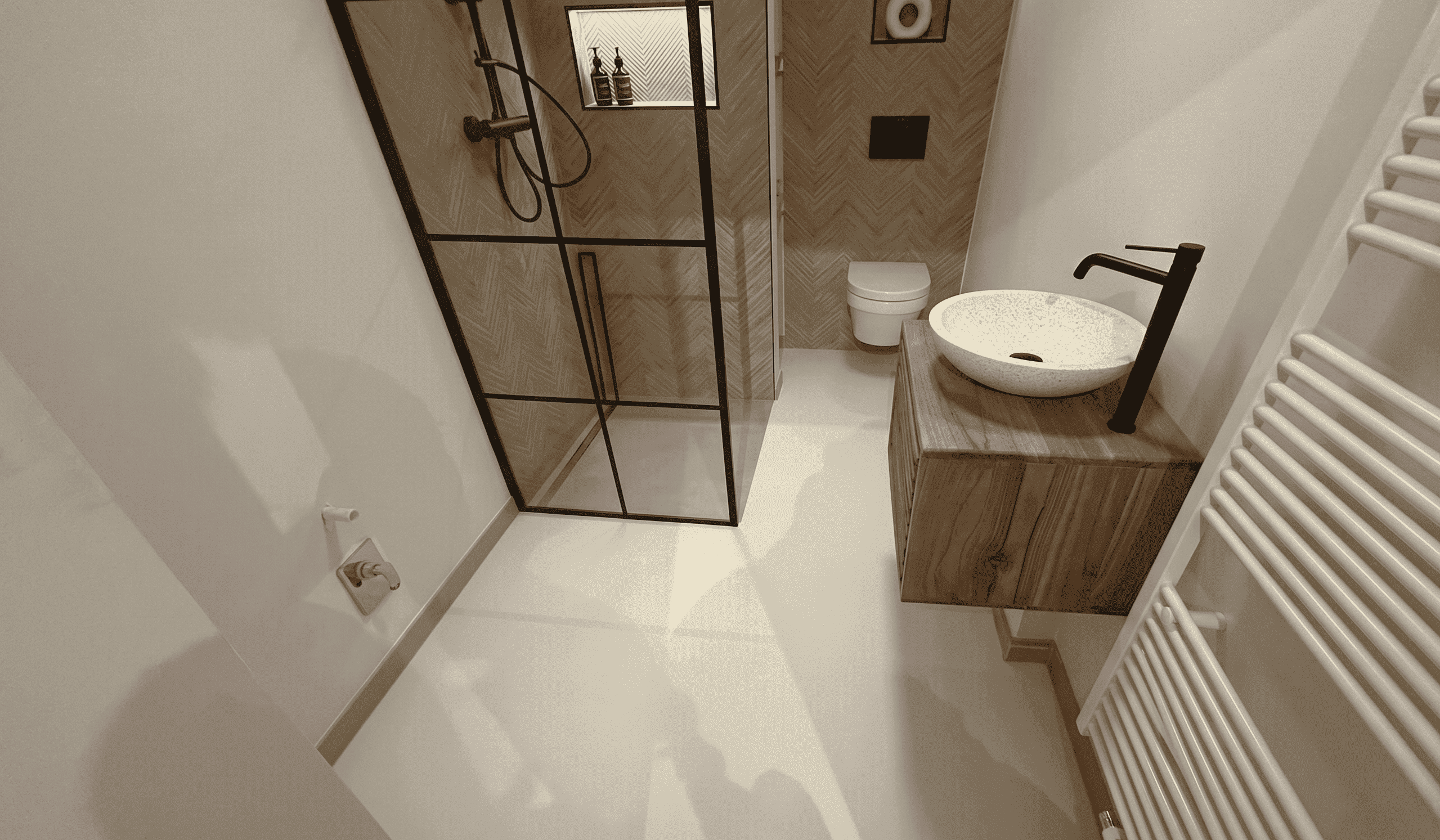 Modernes Badezimmer nach der Sanierung mit fugenlosem Epoxidharz-Boden in elegantem Reinweiß. Die nahtlose, hochglänzende Oberfläche ersetzt den ehemaligen Fliesenboden vollständig und sorgt für ein großzügiges, helles Raumgefühl. In Kombination mit der schwarzen Duschabtrennung, den mattschwarzen Armaturen und dem Waschtisch aus Massivholz entsteht ein zeitloses, hochwertiges Design. 