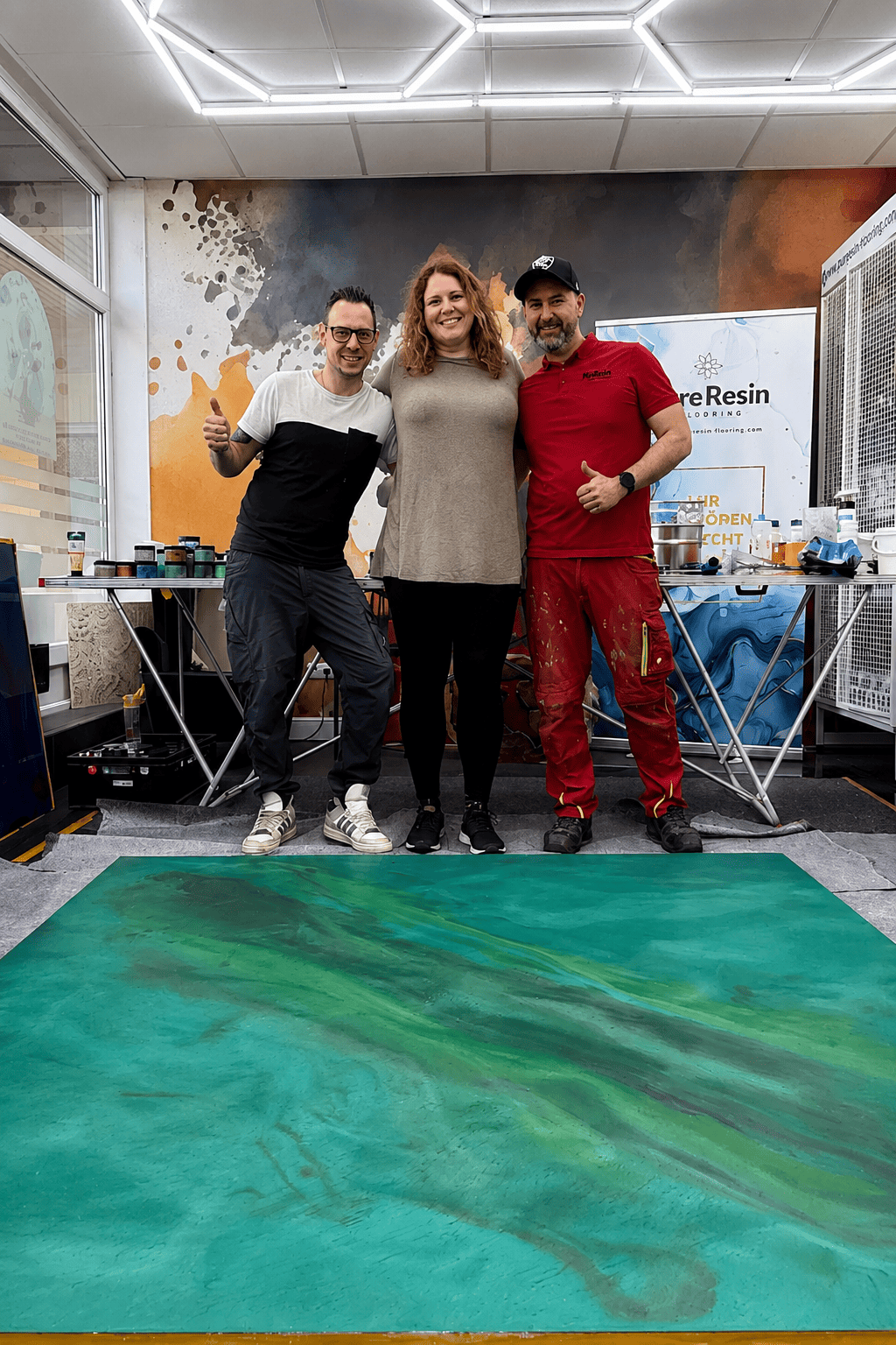 Zwei Teilnehmer und ein Trainer präsentieren nach einem Pure Resin Flooring Workshop eine selbst gestaltete grüne Epoxidharz-Musterplatte.