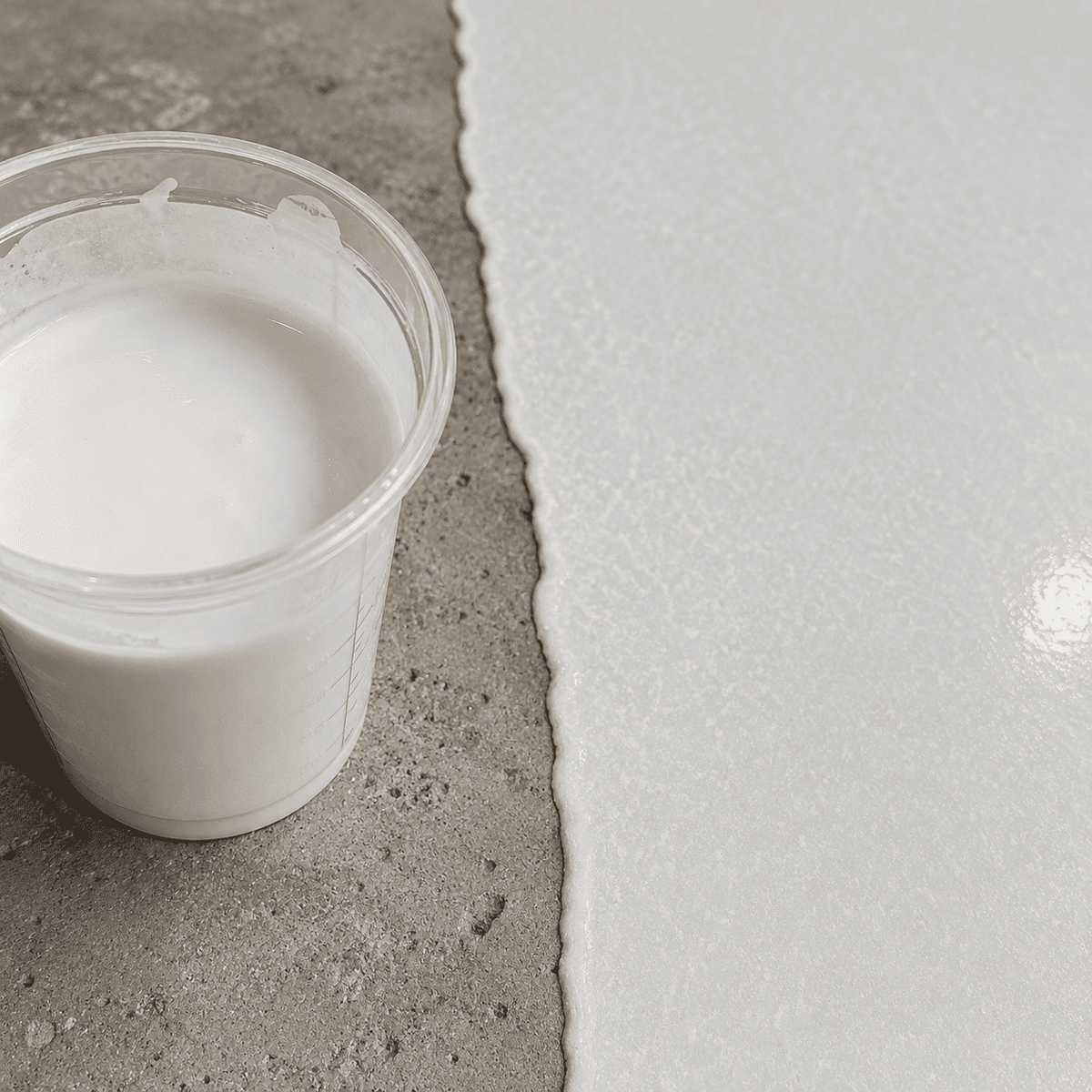 Weißes Epoxidharz im Mischbecher neben einer frisch beschichteten Betonfläche