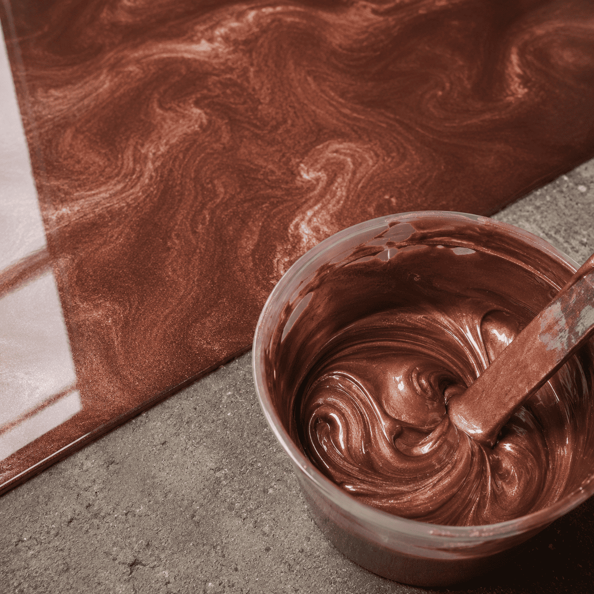 Bronzefarbenes Metallic-Epoxidharz im Mischbecher neben der fertig beschichteten Musterfläche