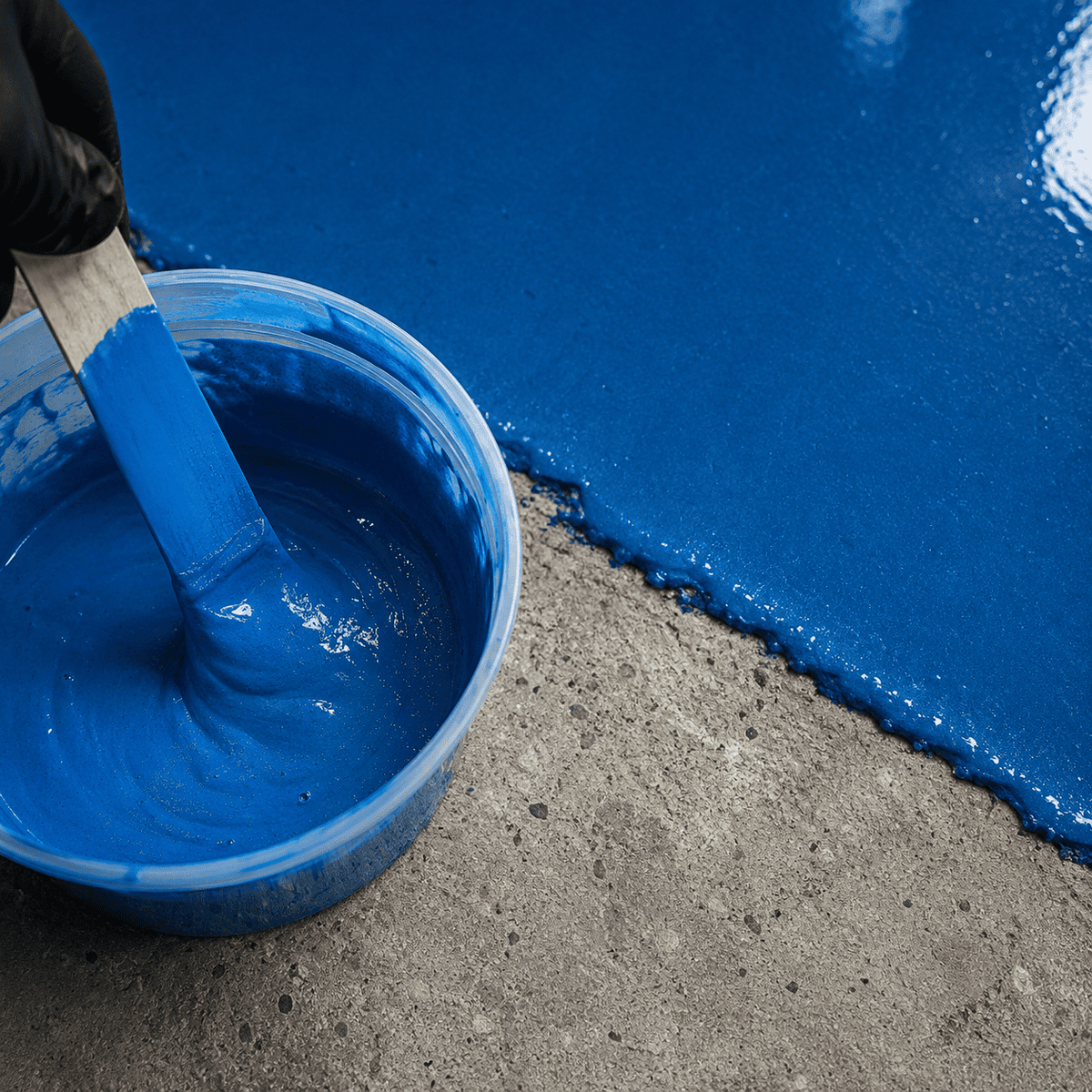 Kobaltblaues Epoxidharz im Mischbecher neben einer frisch beschichteten Betonfläche.