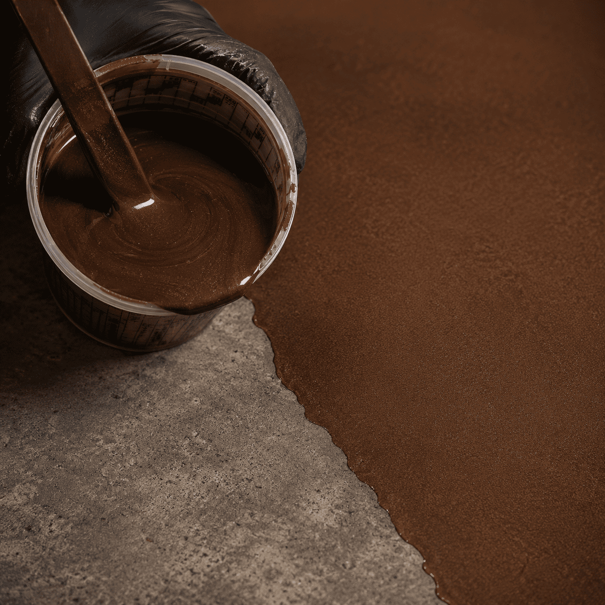 Kupferbraunes Metallic-Epoxidharz im Mischbecher neben einer frisch beschichteten Betonfläche mit edlem Metallglanz und feinem Perleffekt.