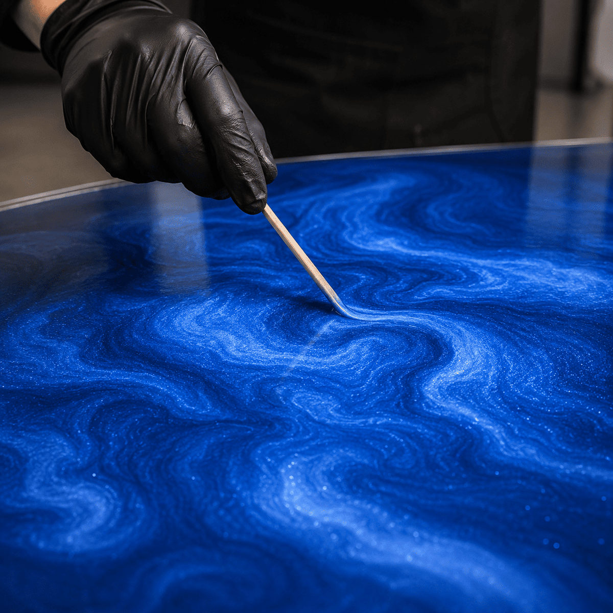 Blaues Metallic-Epoxidharz wird mit einem Holzstab zur markanten Marmorstruktur und lebendigen Tiefenwirkung gestaltet