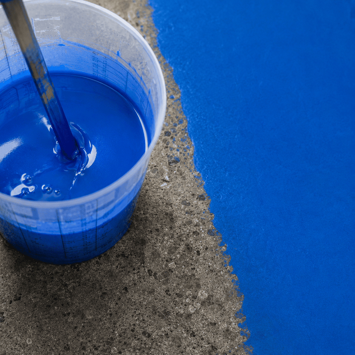 Blaues Epoxidharz im Mischbecher neben einer frisch beschichteten Betonfläche