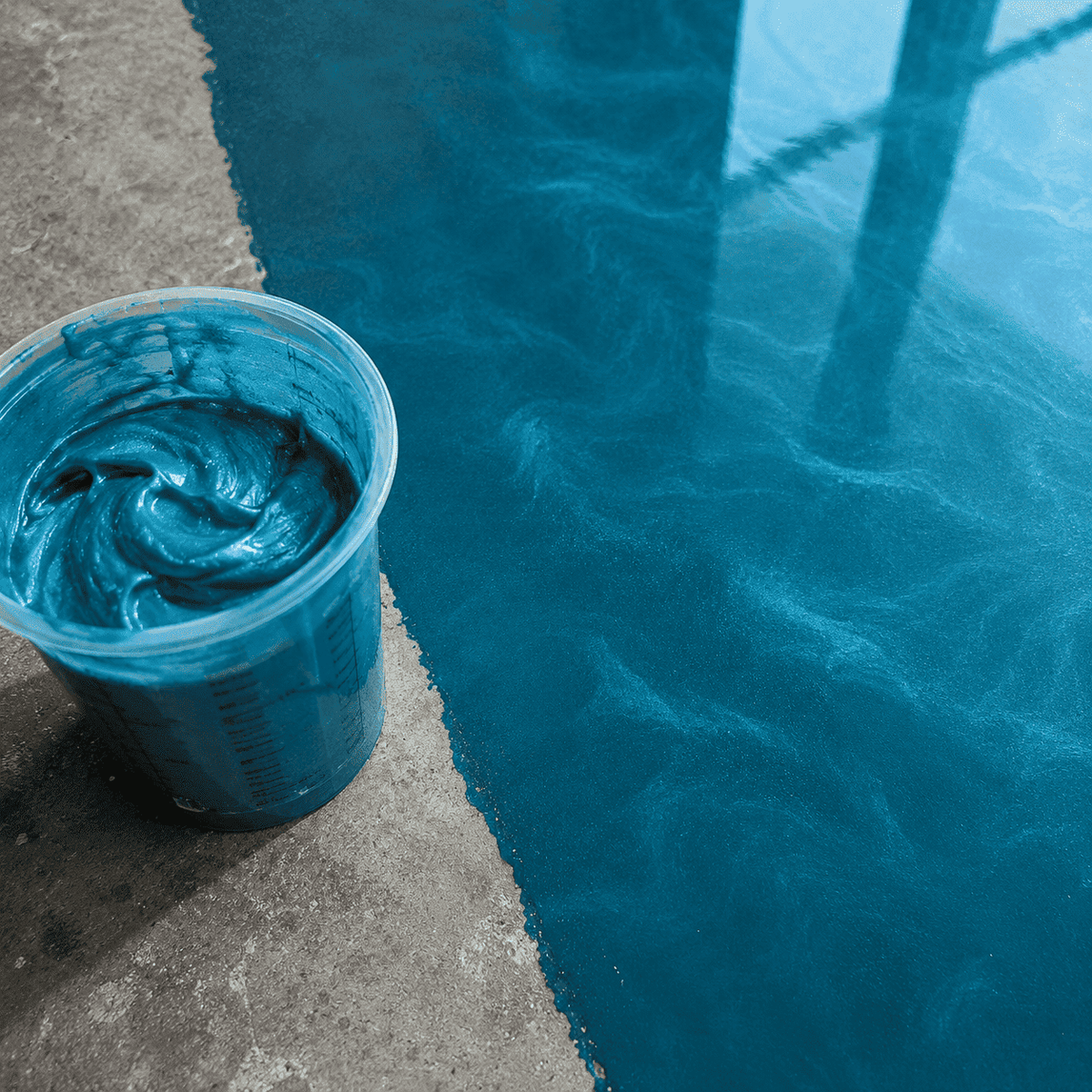 Deep-Ocean-UV Metallic-Epoxidharz im Mischbecher neben einer frisch beschichteten Betonfläche mit intensivem Perleffekt, edler Marmorstruktur und hochglänzender Tiefenwirkung.
