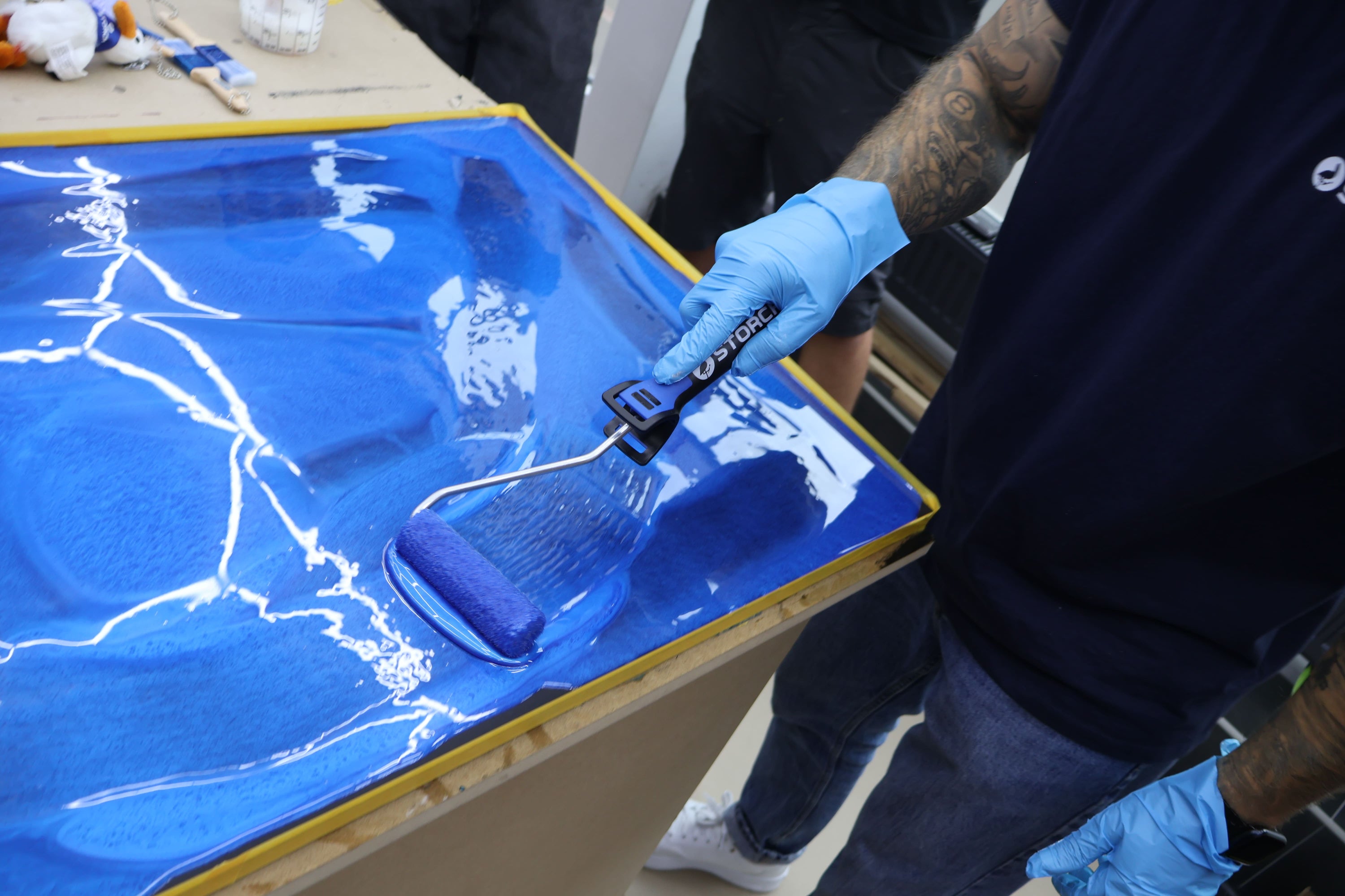 Transparente Versiegelung wird mit einer Rolle auf eine blaue Metallic-Epoxidharz-Musterplatte im Workshop aufgetragen.