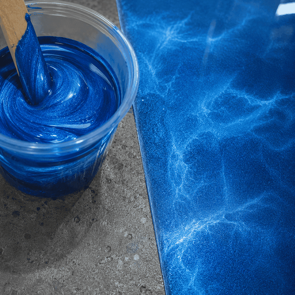 Blaues Metallic-Epoxidharz im Mischbecher und auf Betonboden aufgetragen