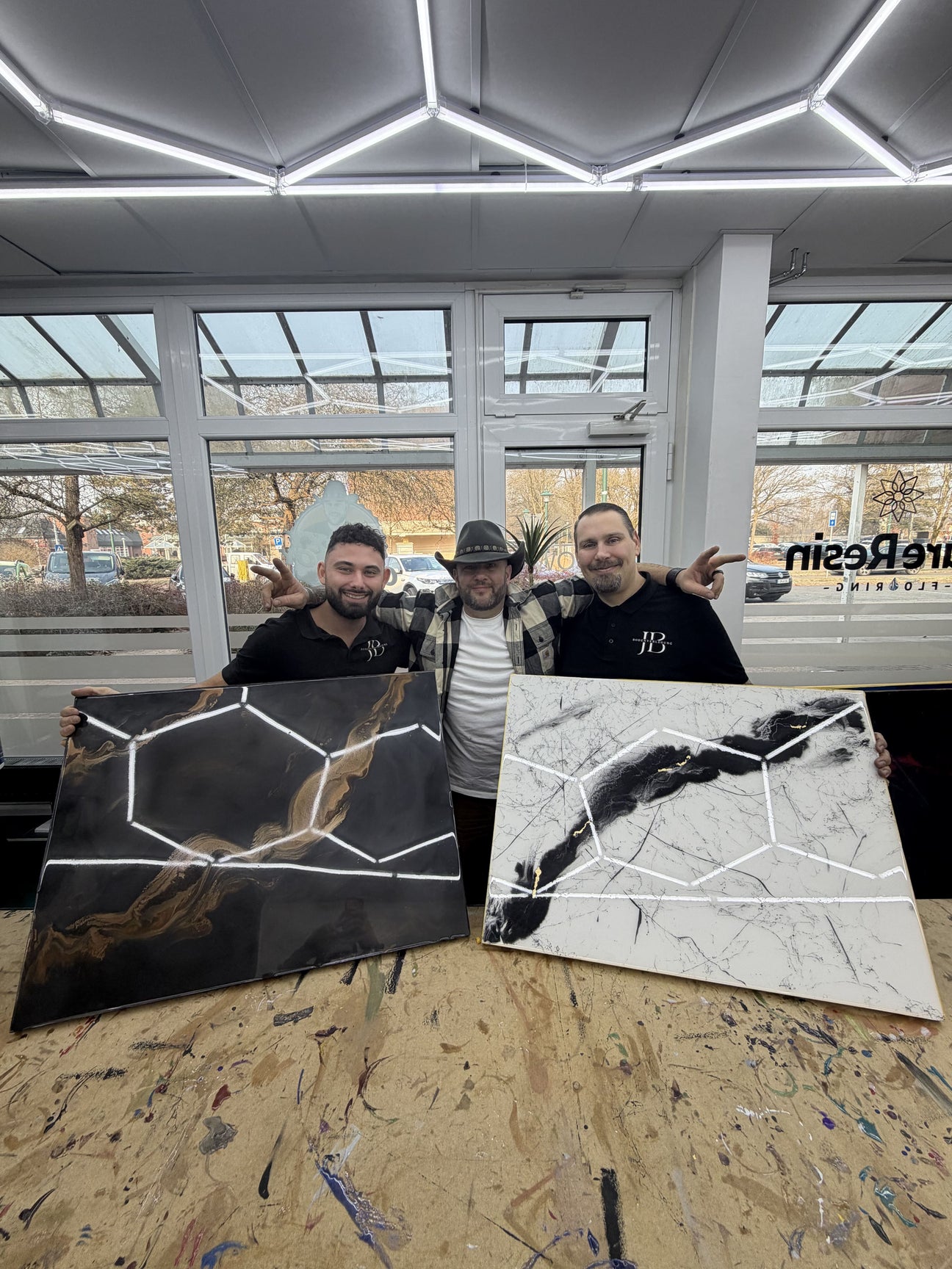 Teilnehmer eines Epoxidharz-Workshops präsentieren zwei selbst gestaltete Musterplatten in schwarzer und weißer Marmoroptik mit Metallic-Effekten.