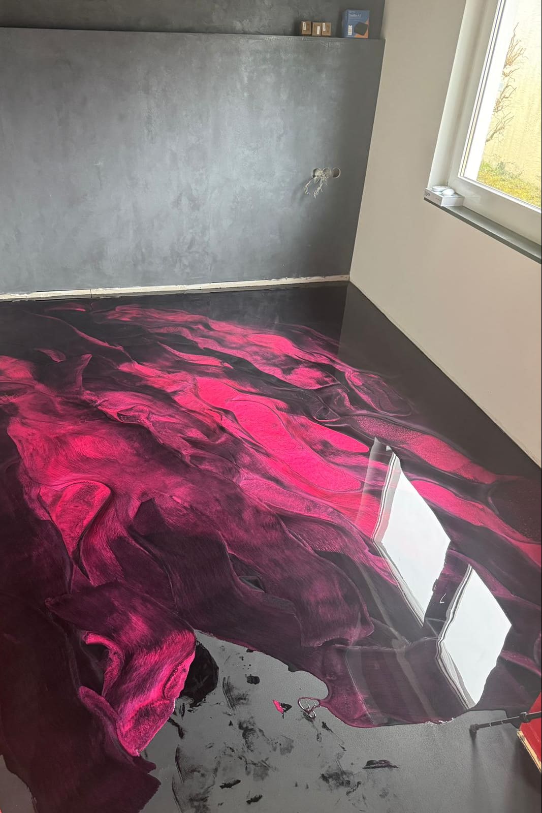 Schwarz-roter Metallic-Epoxidharz-Boden mit intensiven Magenta-Farbverläufen und hochglänzender, fugenloser Oberfläche im modernen Wohnraum.