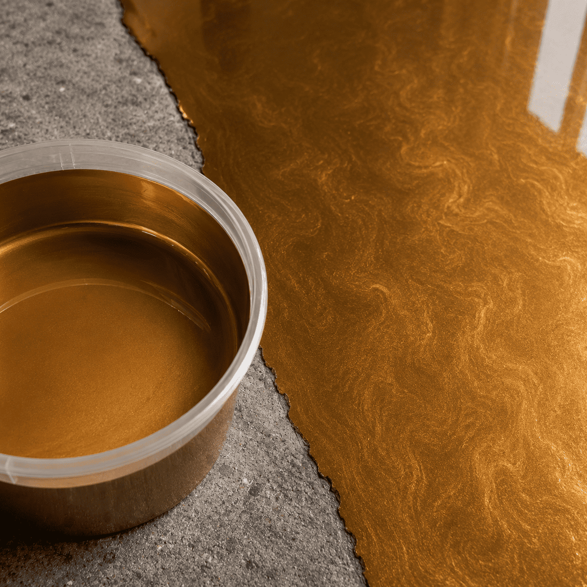 Maya Gold UV Metallic-Epoxidharz im Mischbecher neben einer frisch beschichteten Betonfläche mit edler Goldoptik, luxuriösem Perleffekt, feiner Marmorstruktur und hochglänzender Tiefenwirkung.