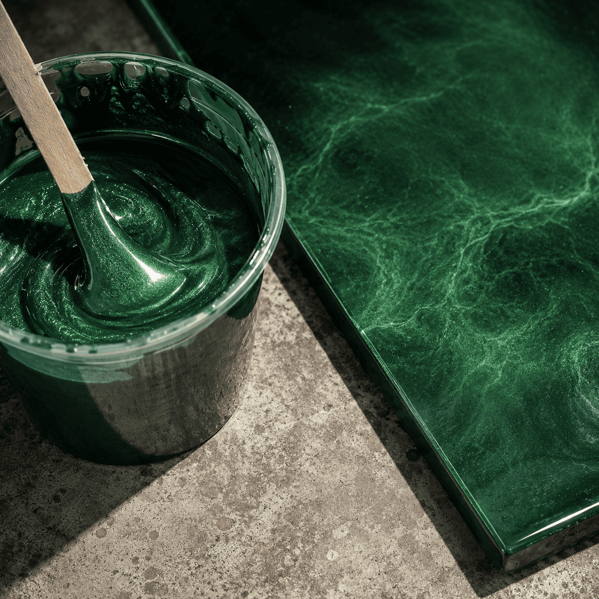 Mighty Jungle UV Metallic-Epoxidharz im Mischbecher neben einer fertigen Musterplatte mit intensiver Smaragdgrün-Optik, luxuriöser Marmorstruktur, brillantem Perleffekt und hochglänzender Tiefenwirkung.