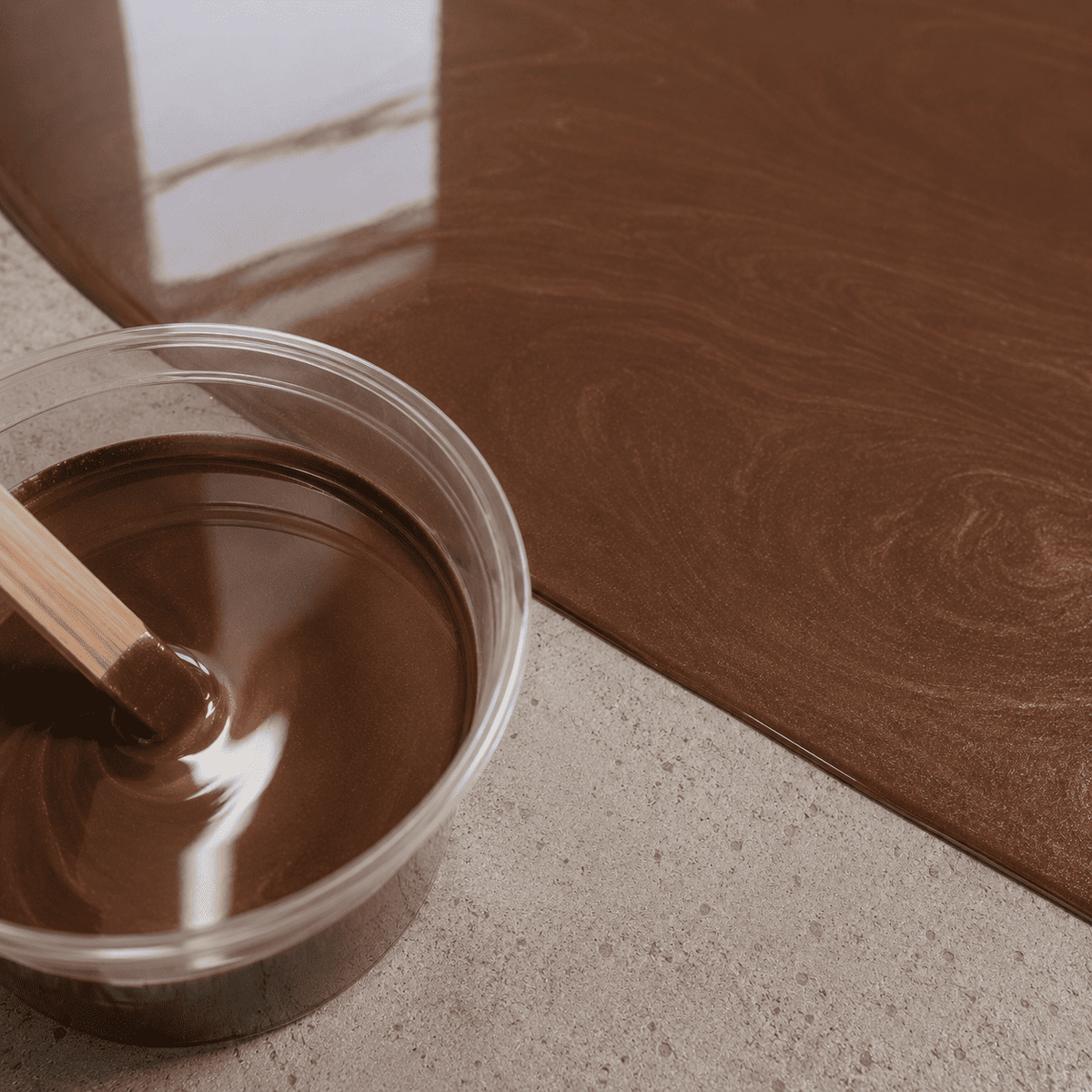 Mud Brown UV Metallic-Epoxidharz im Mischbecher neben einer frisch beschichteten Betonfläche mit warmer Naturstein-Optik, feinem Perleffekt und hochglänzender Tiefenwirkung.