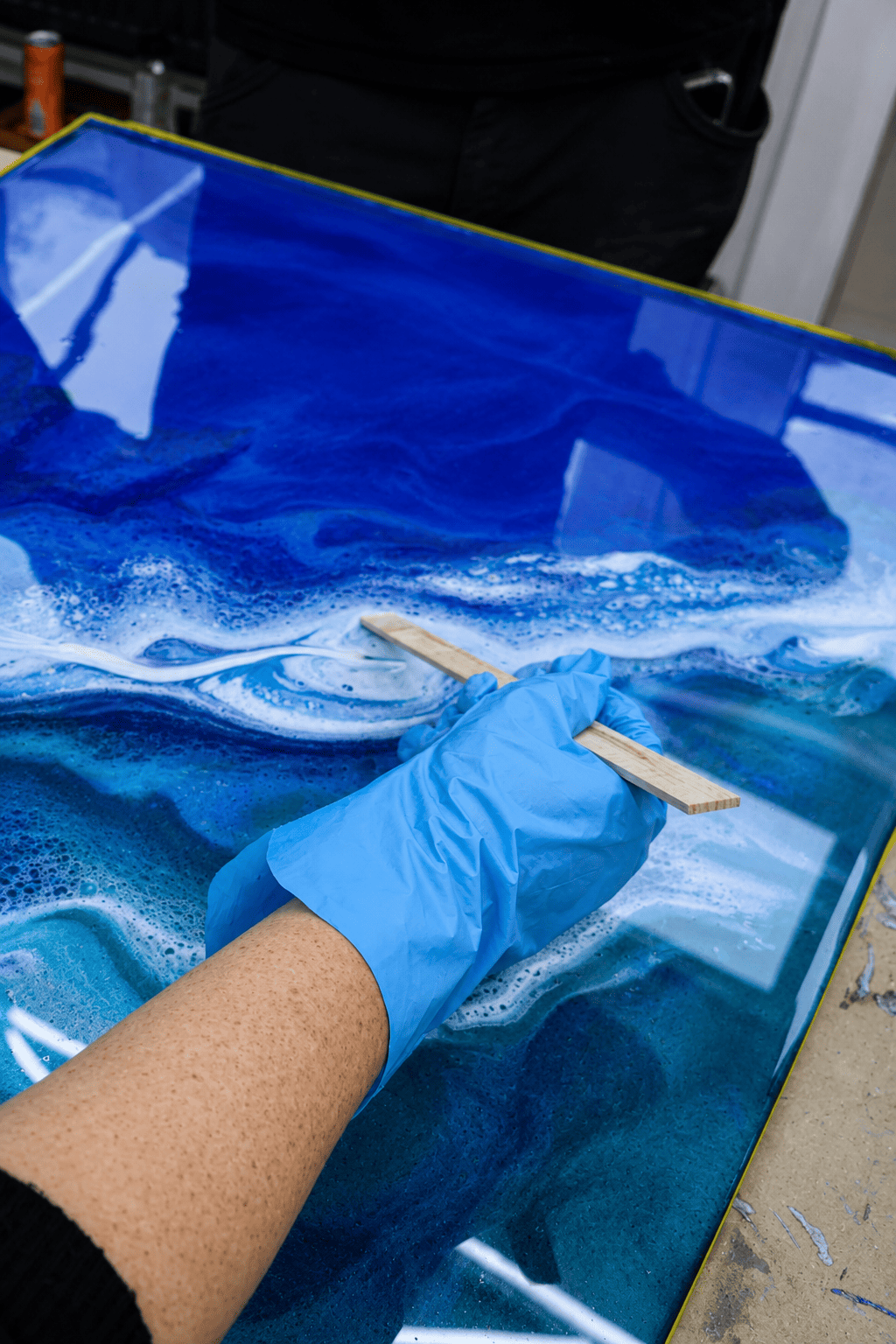 Teilnehmer eines Epoxidharz-Workshops gestaltet eine blaue Metallic-Epoxidharz-Musterplatte mit weißen Wellenstrukturen und professioneller Effekttechnik.