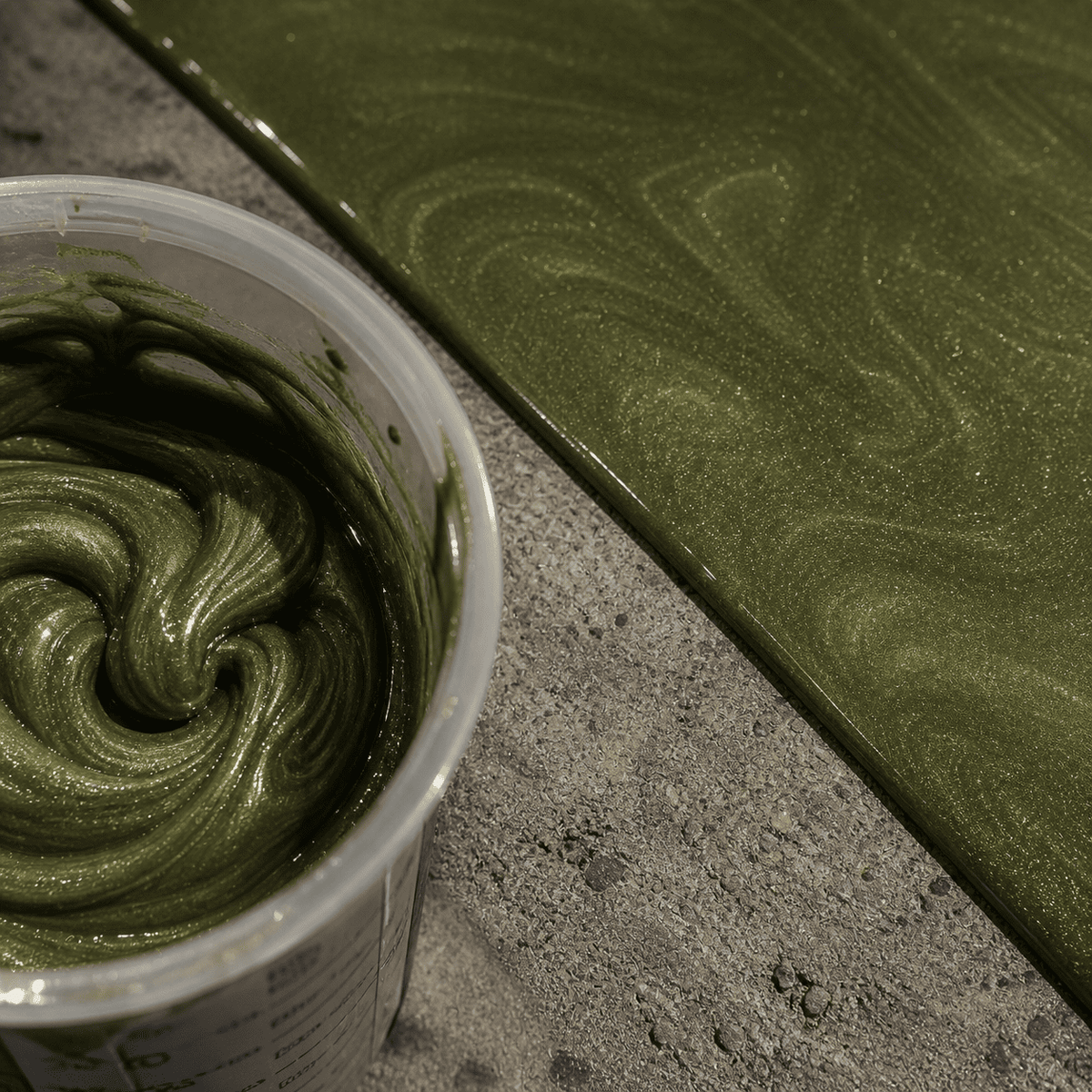 Olivia Green UV Metallic-Epoxidharz im Mischbecher neben einer fertigen Musterplatte mit edler Olivgrün-Optik, feiner Marmorstruktur, brillantem Perleffekt und hochglänzender Tiefenwirkung.