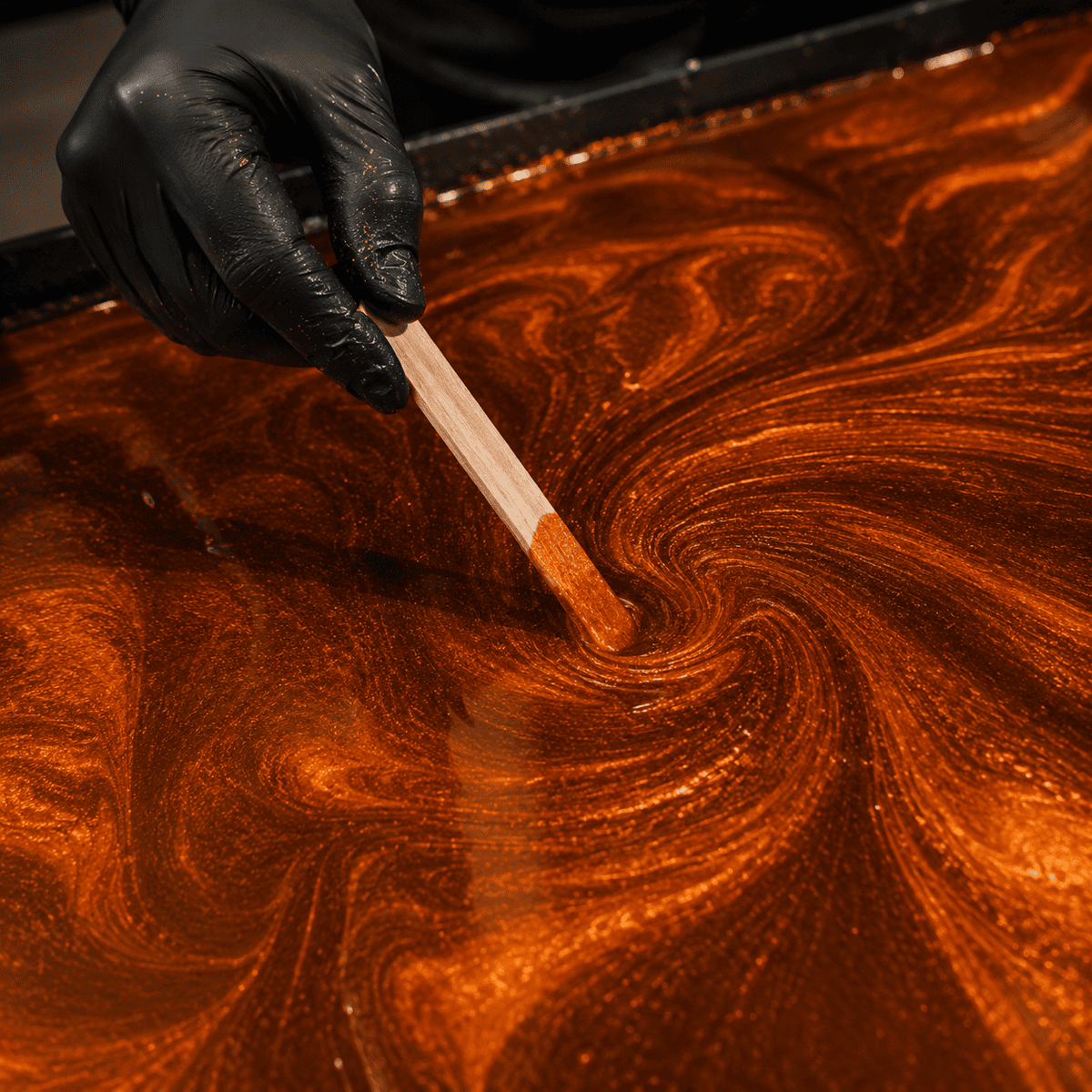 Leuchtend orangefarbenes Metallic-Epoxidharz wird mit einem Holzspatel zu einer ausdrucksstarken Marmorstruktur mit intensivem Perlglanz und faszinierender Tiefenwirkung gestaltet.
