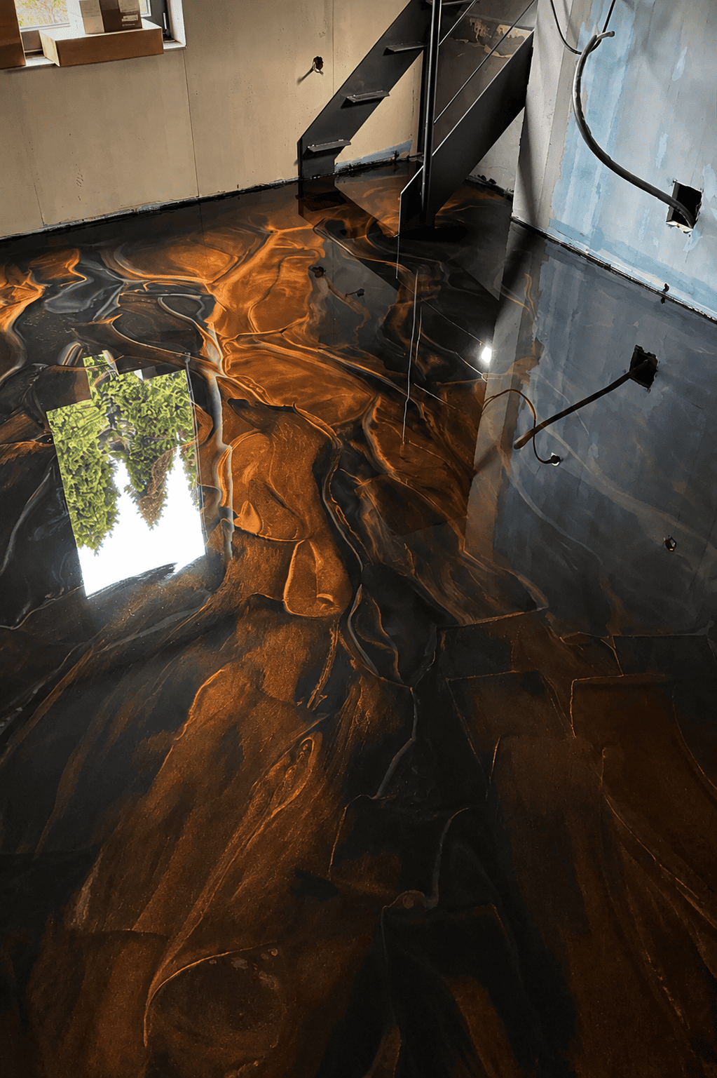 Schwarzer Metallic-Epoxidharz-Boden mit kupferfarbenen Marmoreffekten und fugenloser Hochglanzoberfläche unter einer modernen Stahltreppe.