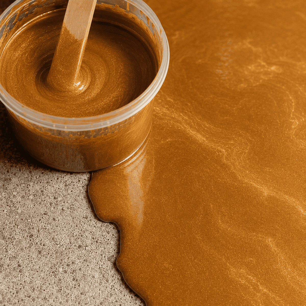 Satin Gold UV Metallic-Epoxidharz im Mischbecher neben einer frisch beschichteten Betonfläche mit edler Goldoptik, luxuriösem Perleffekt, feiner Marmorstruktur und hochglänzender Oberfläche.