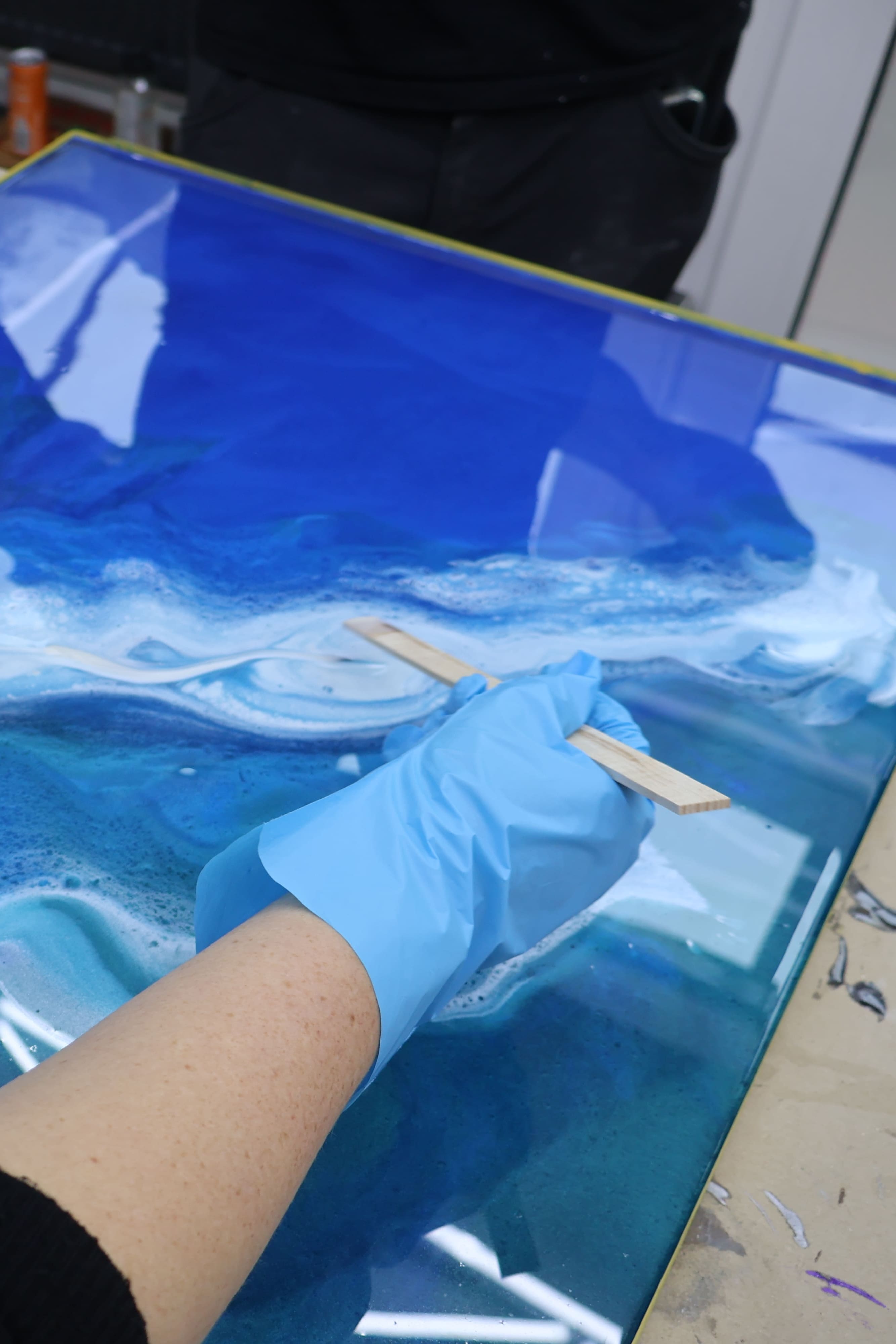Teilnehmer eines Epoxidharz-Workshops gestaltet eine blaue Metallic-Epoxidharz-Musterplatte mit weißen Wellenstrukturen und professioneller Effekttechnik.