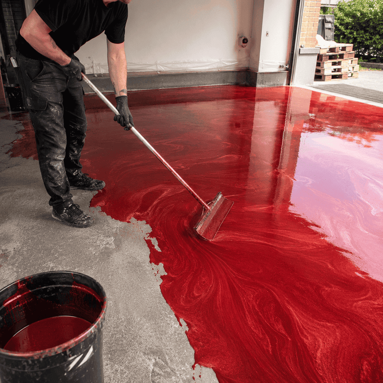 Ein Mann streicht einen Beton Boden in roter Farbe mit einem Farbroller