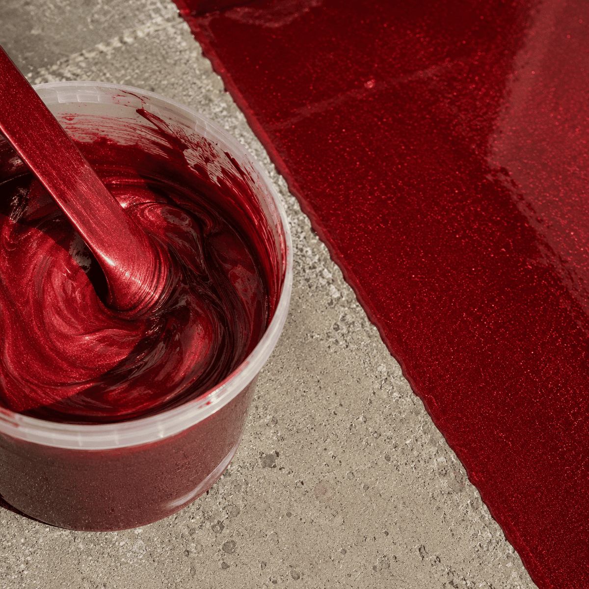 Soulfire Metallic-Epoxidharz im Mischbecher neben einer frisch beschichteten Betonfläche mit intensivem Rotton, brillantem Perleffekt und hochglänzender Tiefenwirkung.