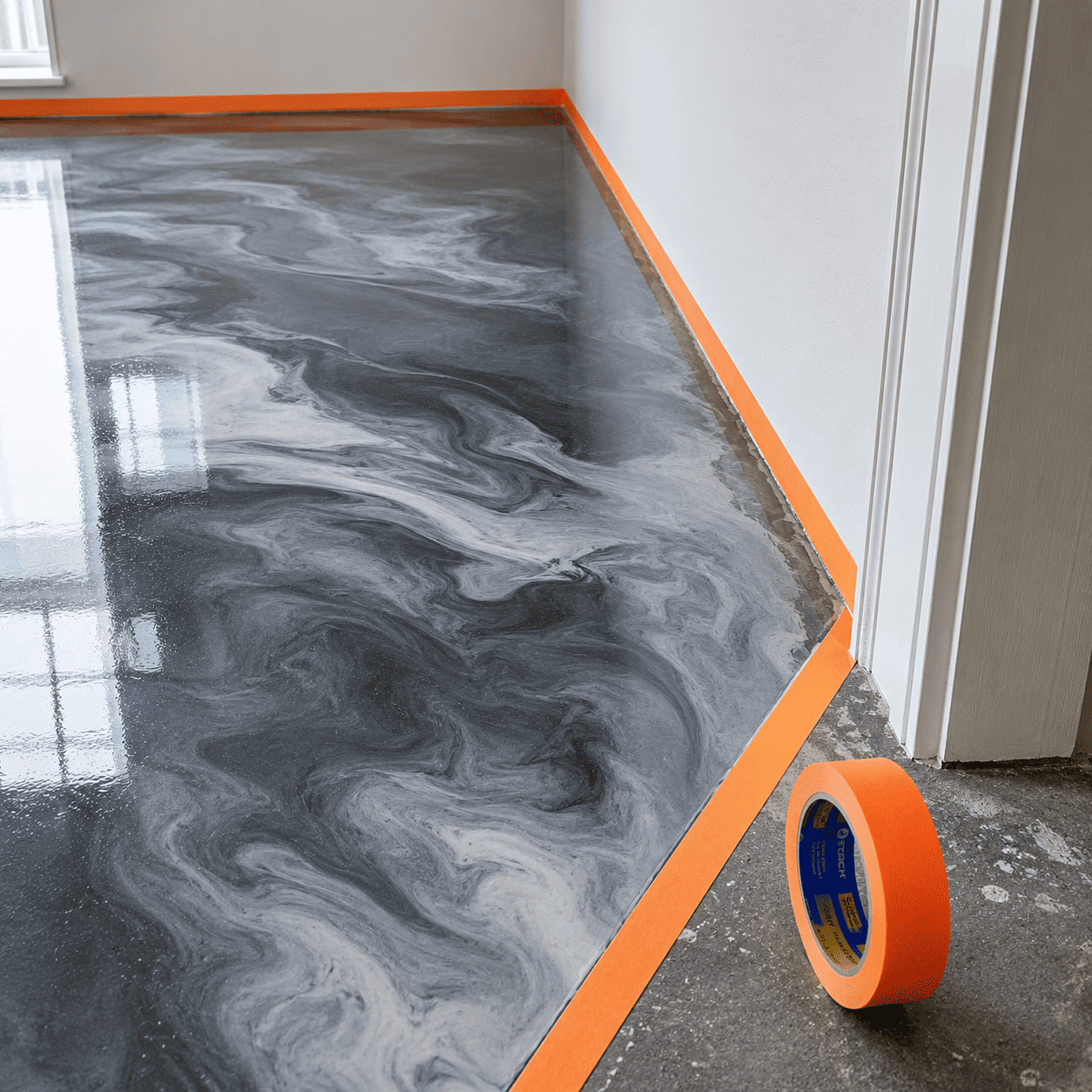 Orangenes Klebeband klebt auf am Rand eines grau beschichteten Boden zum Abkleben der Ränder