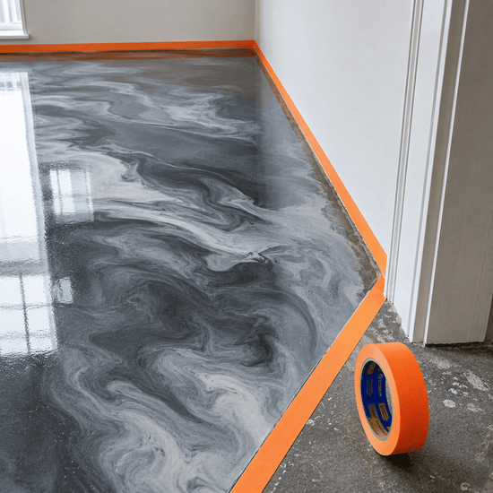 Orangenes Klebeband klebt auf am Rand eines grau beschichteten Boden zum Abkleben der Ränder