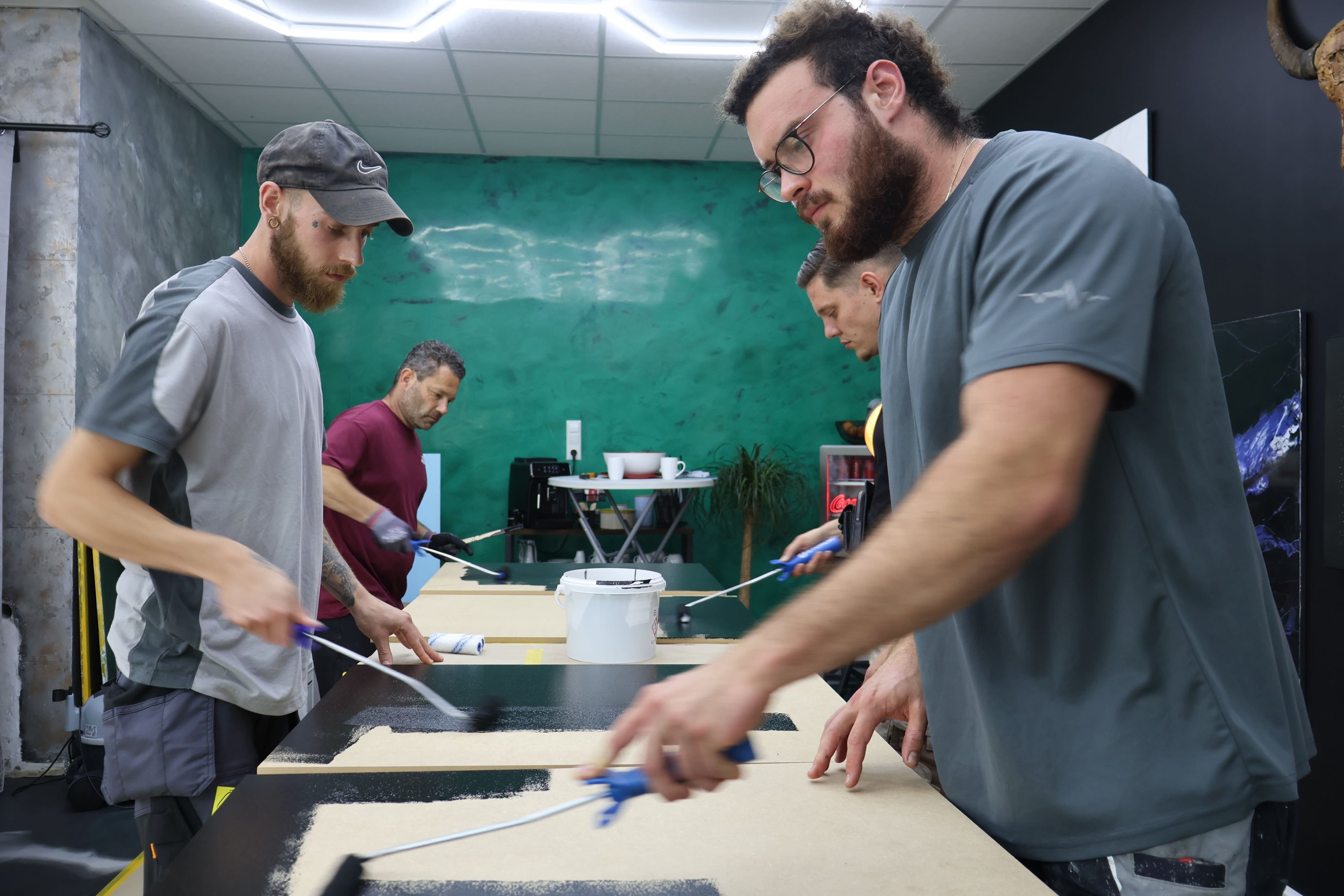 Teilnehmer eines Epoxidharz-Workshops tragen schwarze Epoxidharz-Grundierung mit Farbrollen auf Musterplatten auf und üben die professionelle Verarbeitung.